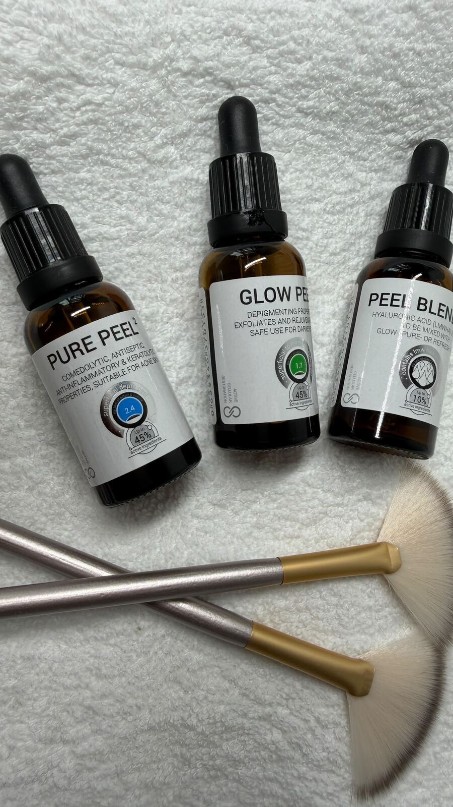 Three amber dropper bottles of clinical peel solution beside fan brushes